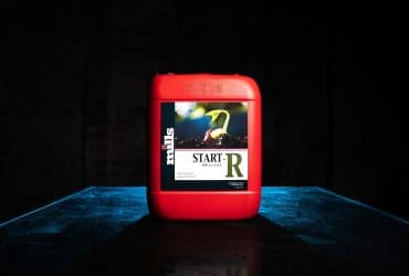 Red container of Mills Start-R placed on blue-lit tabletop, spotlighting young cannabis seedling graphic on label